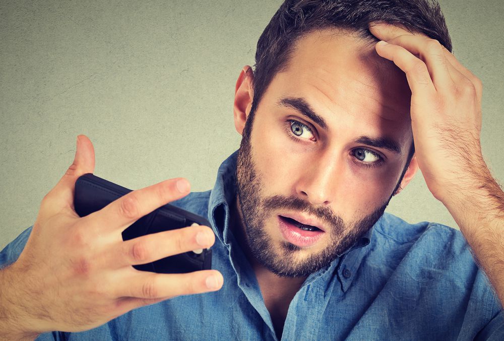 Closeup portrait, shocked man feeling head, surprised he is losing hair, receding hairline, bad news isolated on gray wall background. Negative facial expressions, emotion feeling